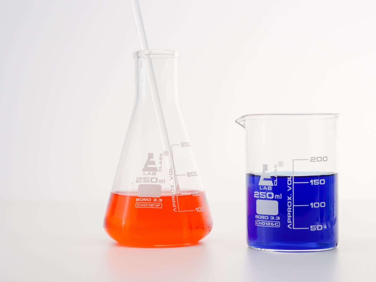 Two laboratory beakers holding orange and blue liquid, side by side for comparison.