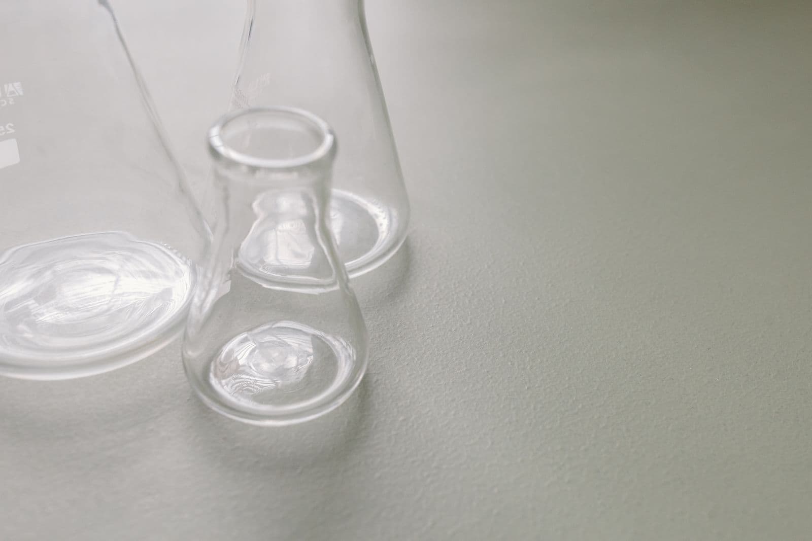 Two clear glass laboratory flasks of different shapes standing side by side on a pale surface.