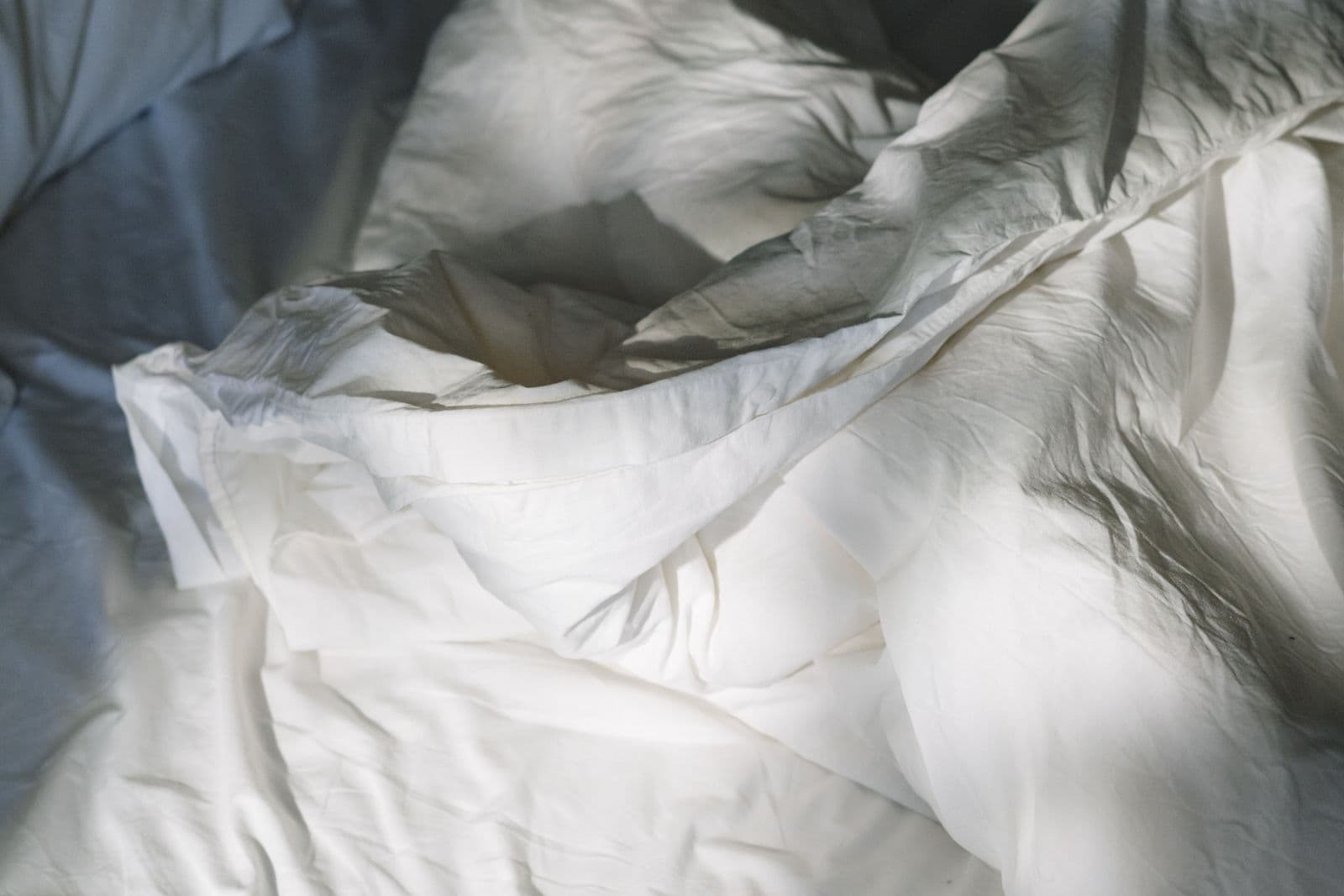 Soft white linen sheets on a bed bathed in warm morning light through a window.