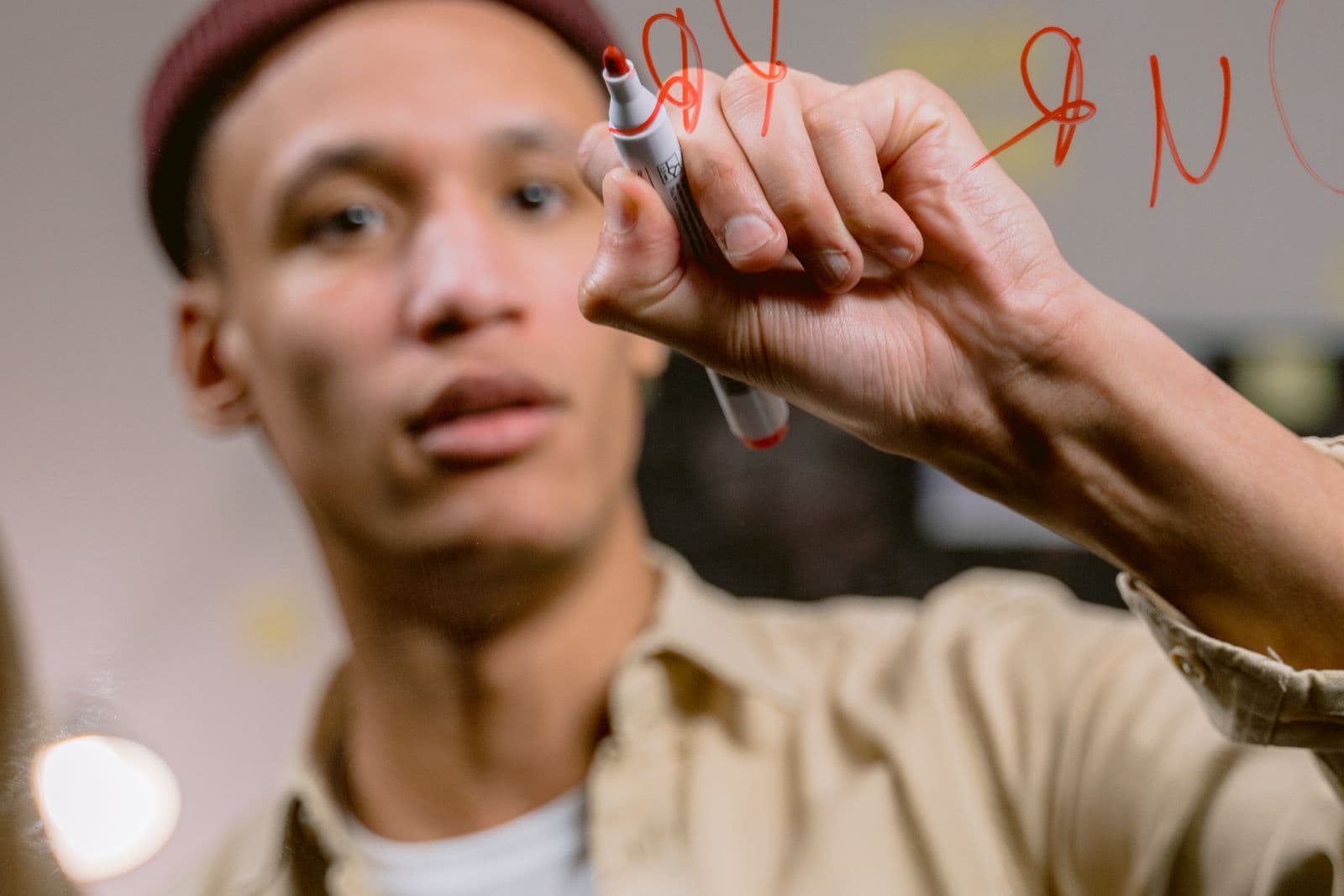 A person thoughtfully writing on a glass surface with a marker in warm indoor light.