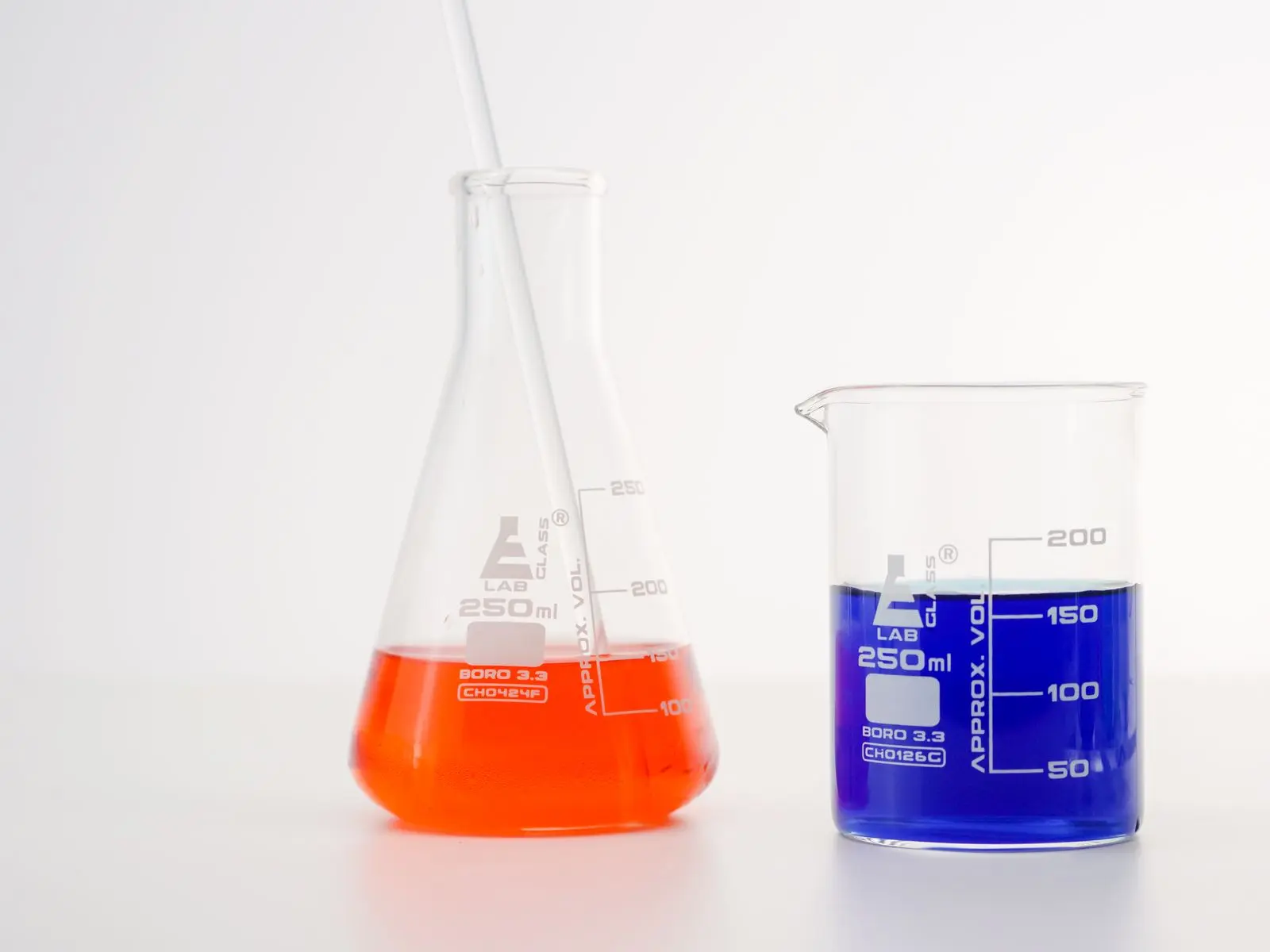 Two laboratory beakers holding orange and blue liquid, side by side for comparison.