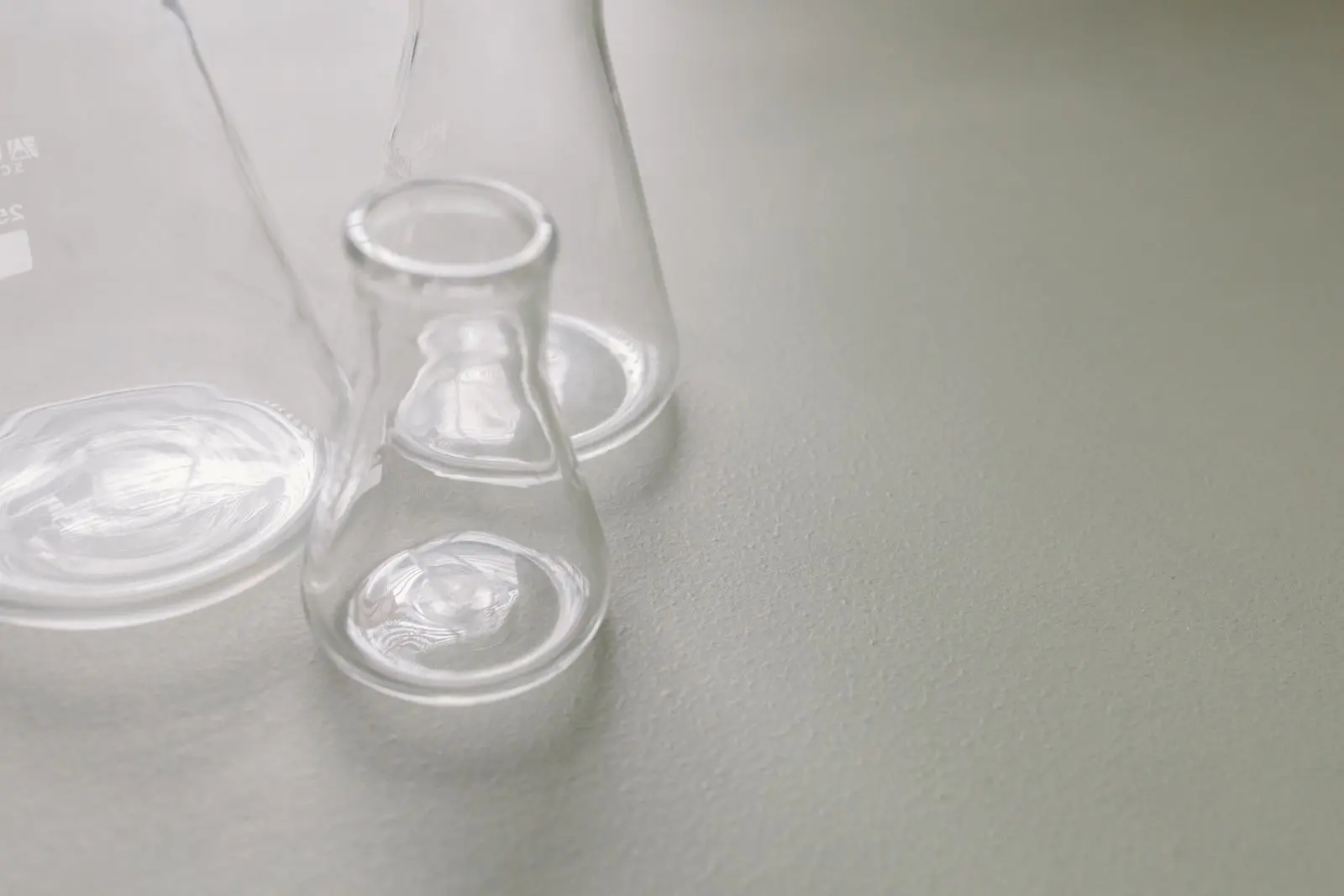 Two clear glass laboratory flasks of different shapes standing side by side on a pale surface.