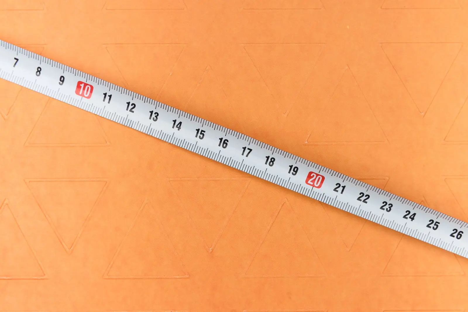 A tailor's tape measure laid diagonally across a textured orange surface.