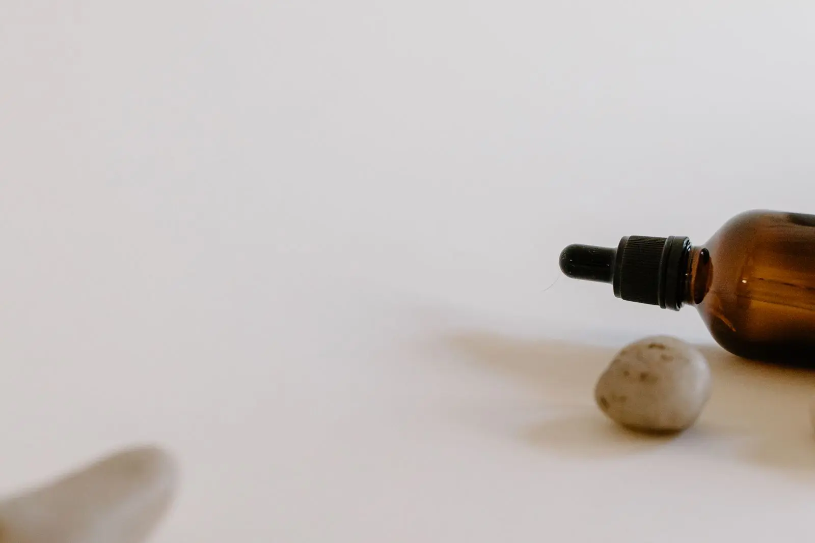 An amber glass dropper bottle beside smooth river stones in soft natural light.