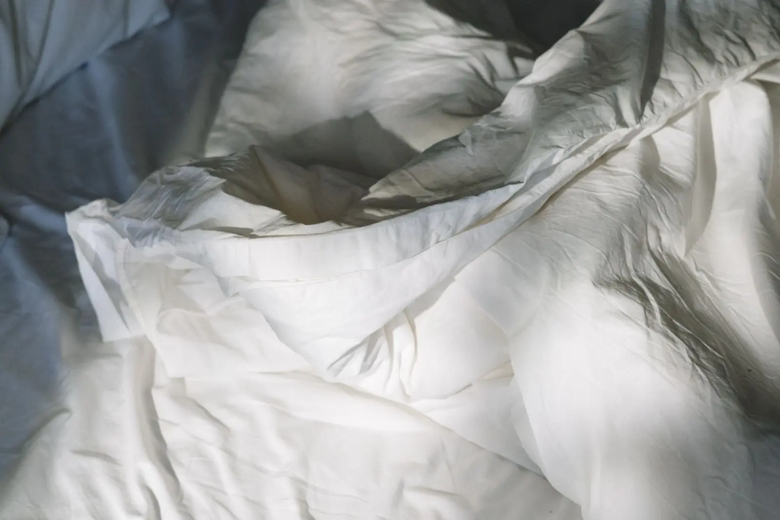 Soft white linen sheets on a bed bathed in warm morning light through a window.