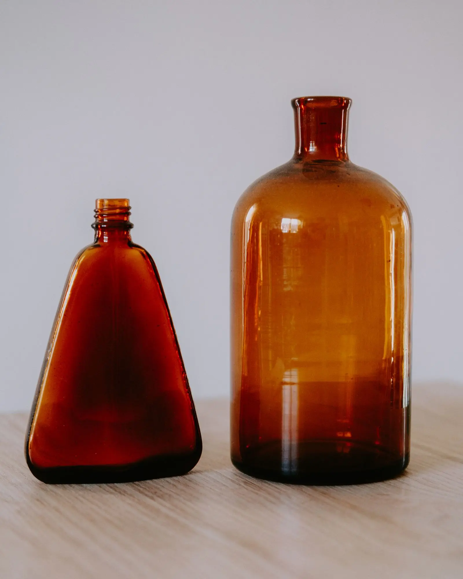 A single amber glass bottle with a young plant cutting rooting in water on an outdoor table.