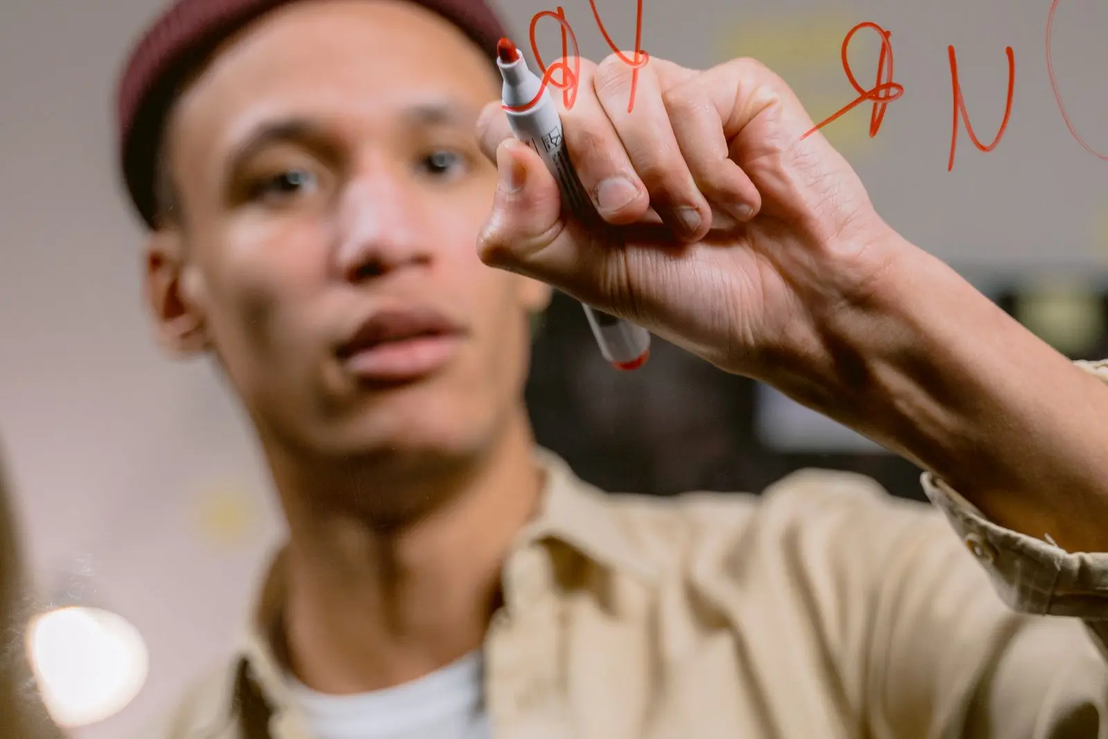 A person thoughtfully writing on a glass surface with a marker in warm indoor light.