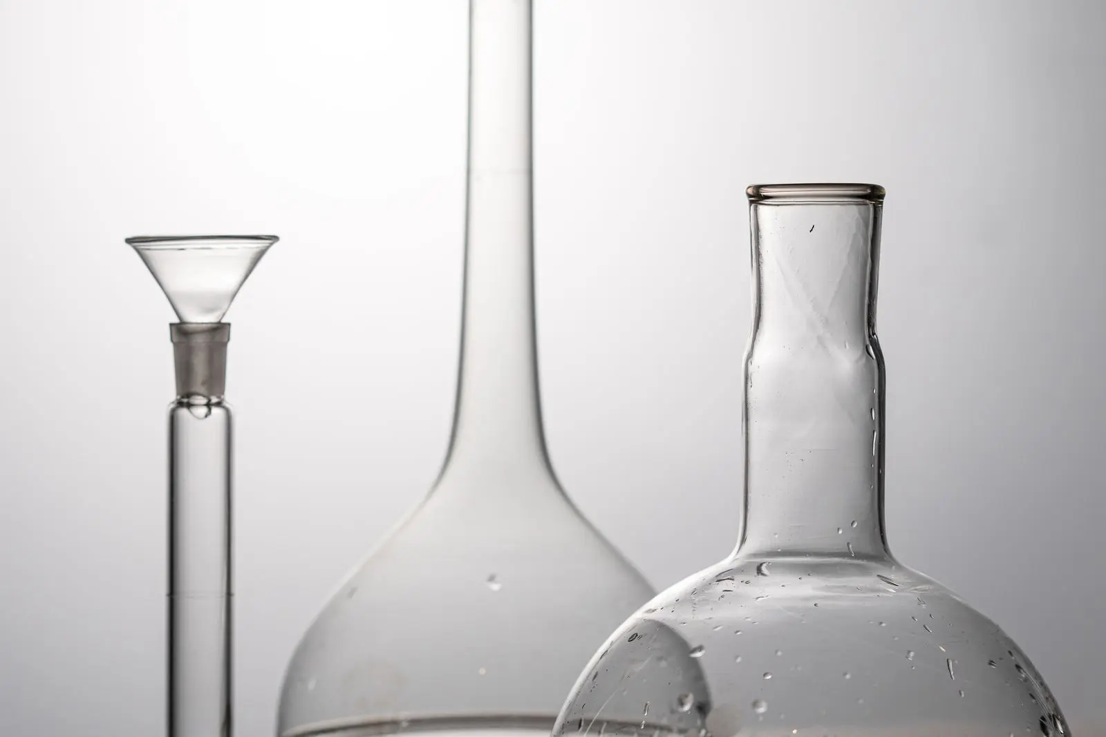 Three clean laboratory flasks with clear liquid on a wooden surface in soft studio light.