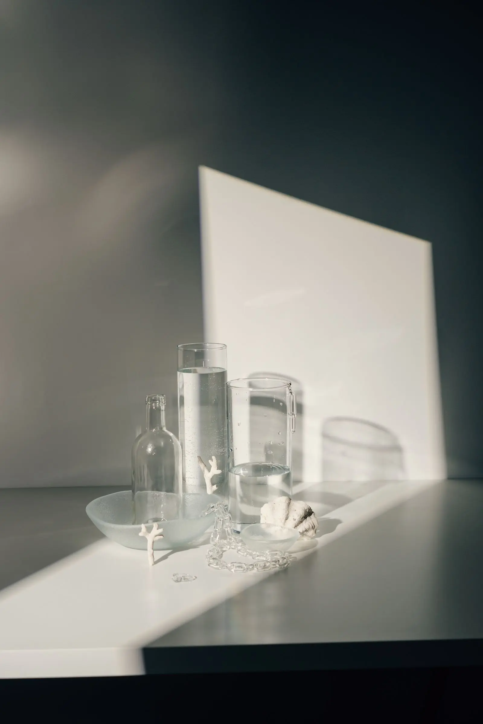 A glass bottle and two water-filled cylinders arranged with coral fragments in soft daylight.