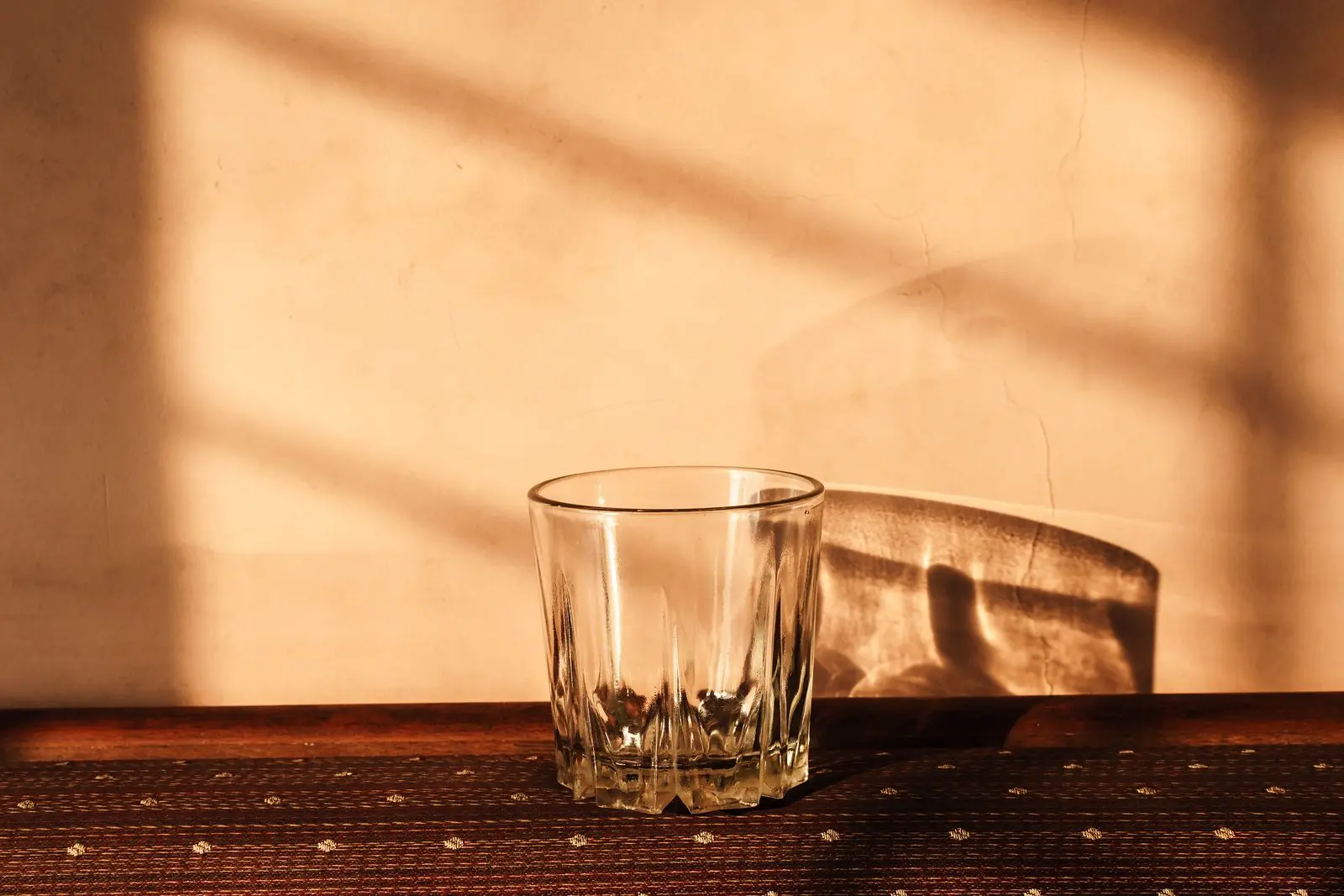 A glass tumbler beside a chair, both cast in warm evening light and shadow.