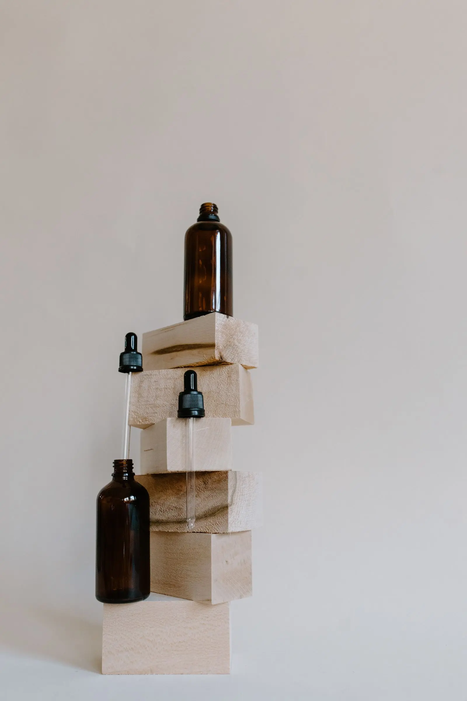 Amber glass dropper bottles balanced on stacked pale wooden blocks.