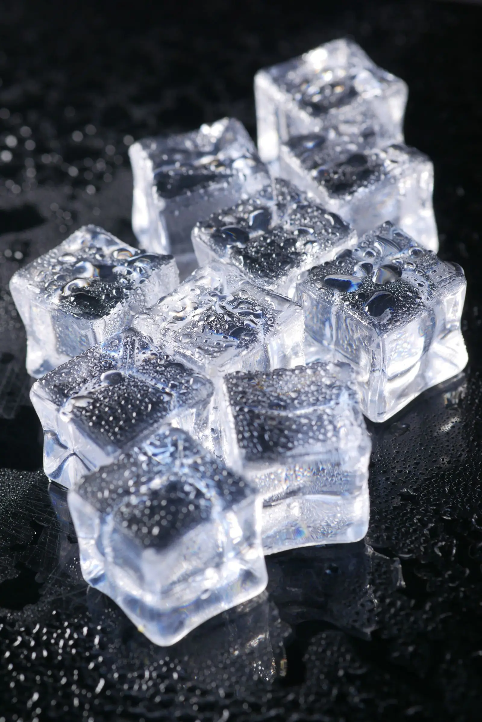 Clear ice cubes glistening on a dark, water-beaded surface.