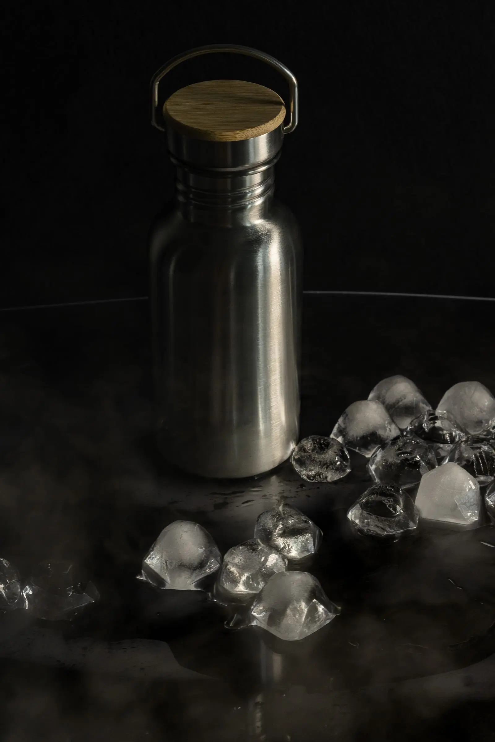 A stainless steel bottle standing among scattered ice cubes against a dark background.